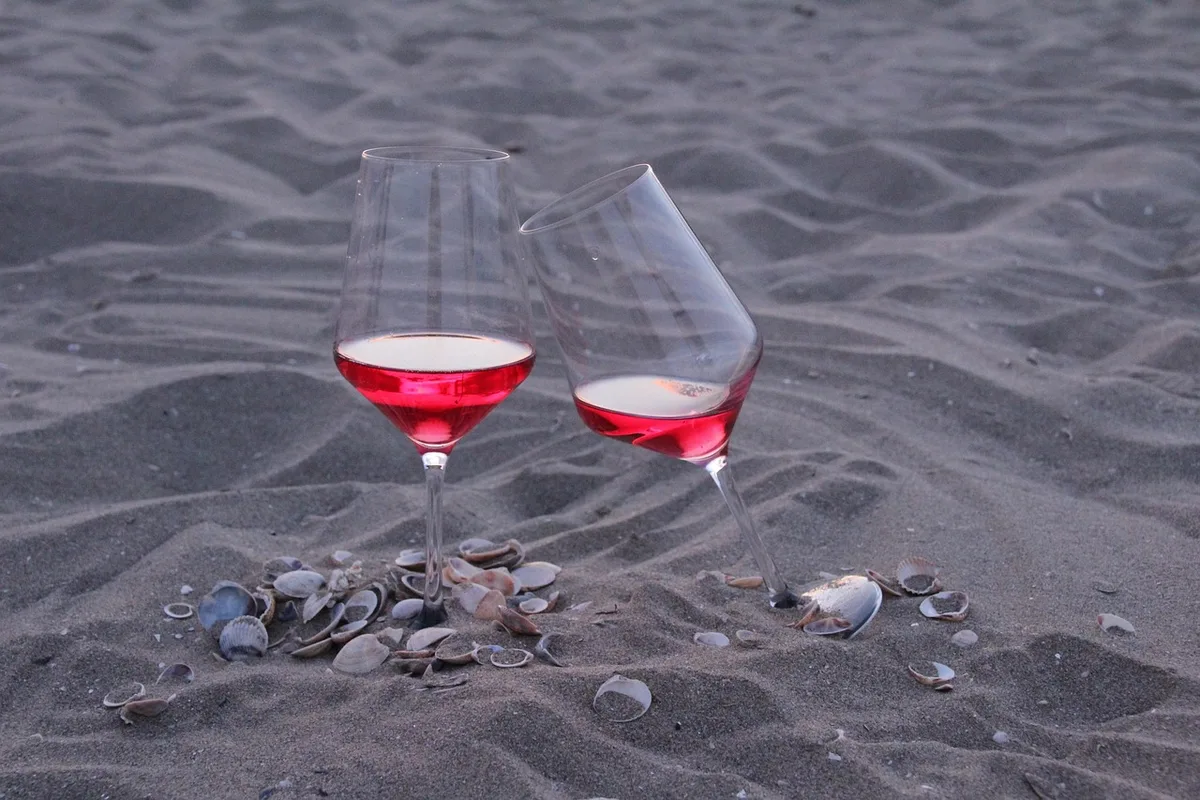 Clean kitchen table with two generic wine glasses, a measuring glass, and a pamphlet about health risks; daylight interior, hands placing one glass down