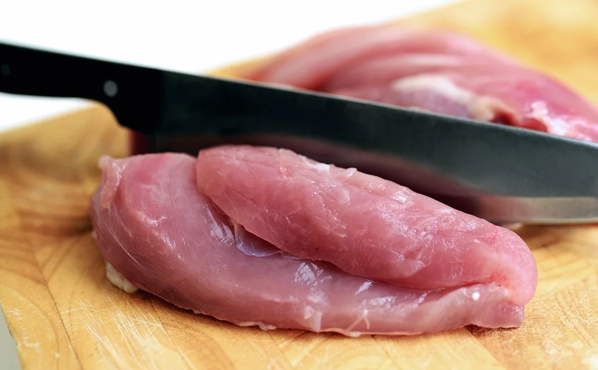 a neatly wrapped assortment of unnamed raw meat cuts on butcher paper with a small eco-friendly tag and kitchen tools nearby