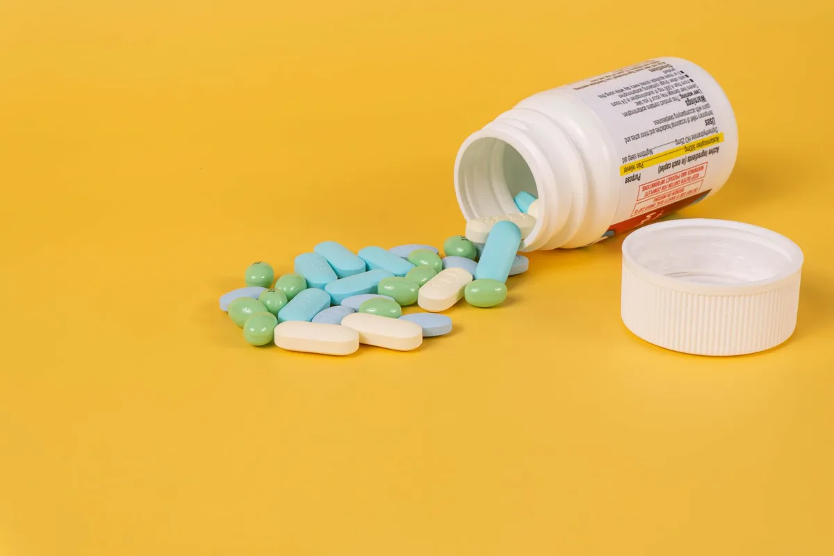 close-up of hands holding a generic pill bottle and a glass of water on a bright table, no label visible