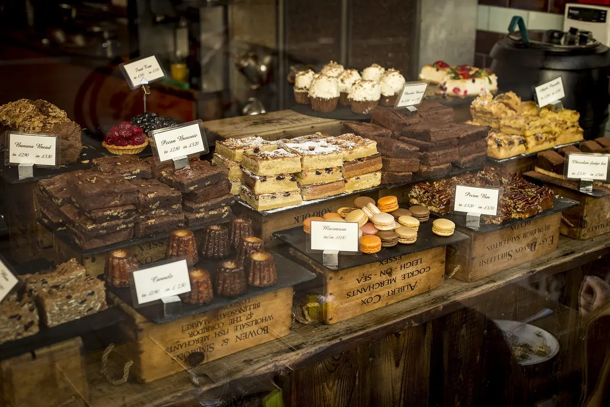 A sunlit butcher's counter with an assortment of unbranded cuts displayed on wooden boards, herbs nearby and a handwritten chalkboard price out of frame