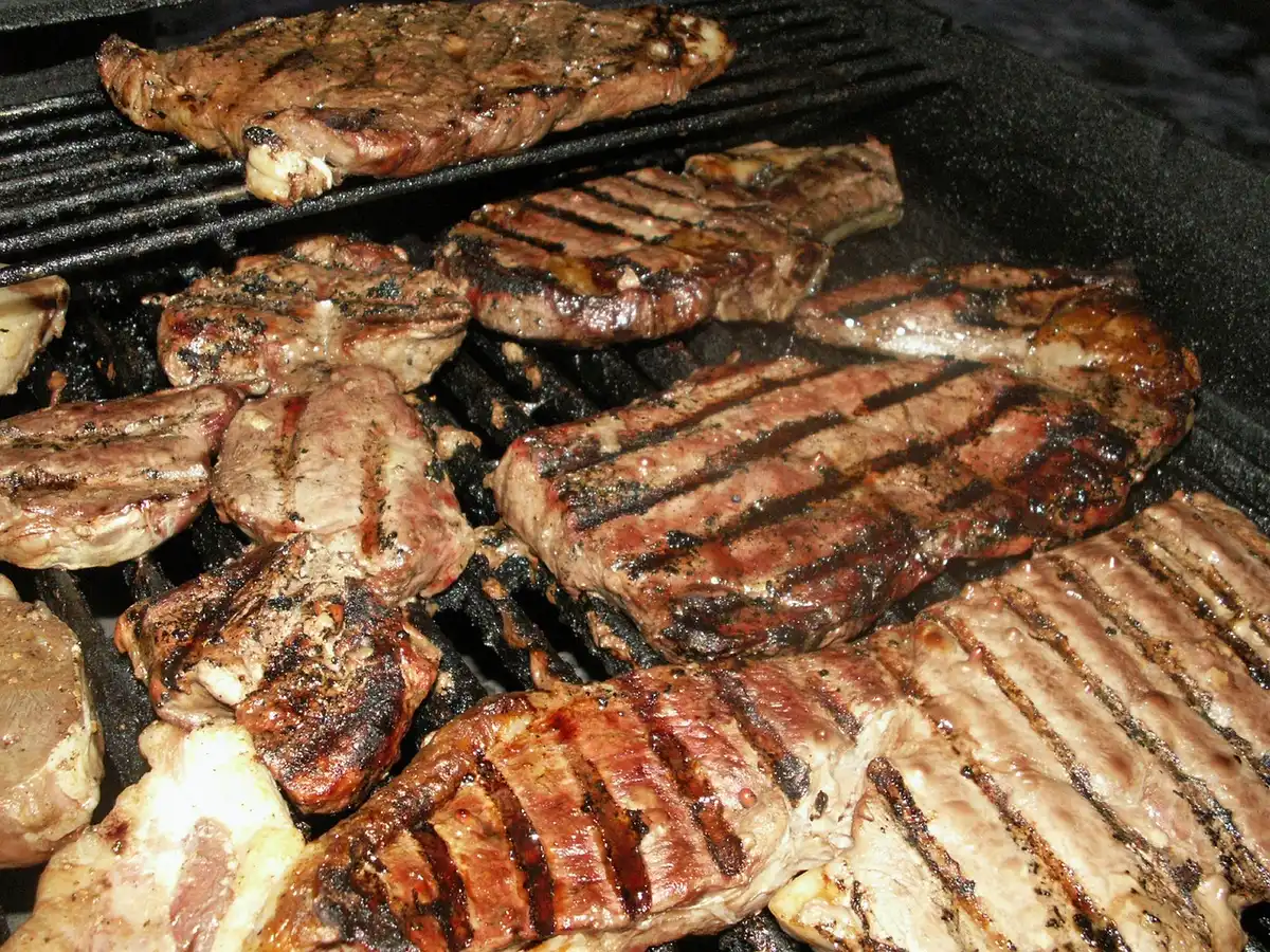 Close-up of a pair of hands slicing an unbranded piece of cured meat on a wooden board, sprigs of rosemary at the edge, natural daylight