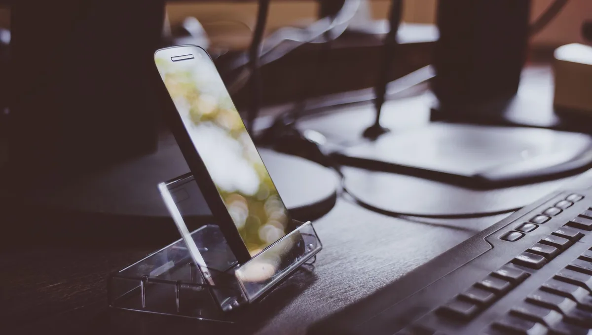 Close-up of hands holding a smartphone over a desk with documents and a pen, screen darkened to suggest app unavailability