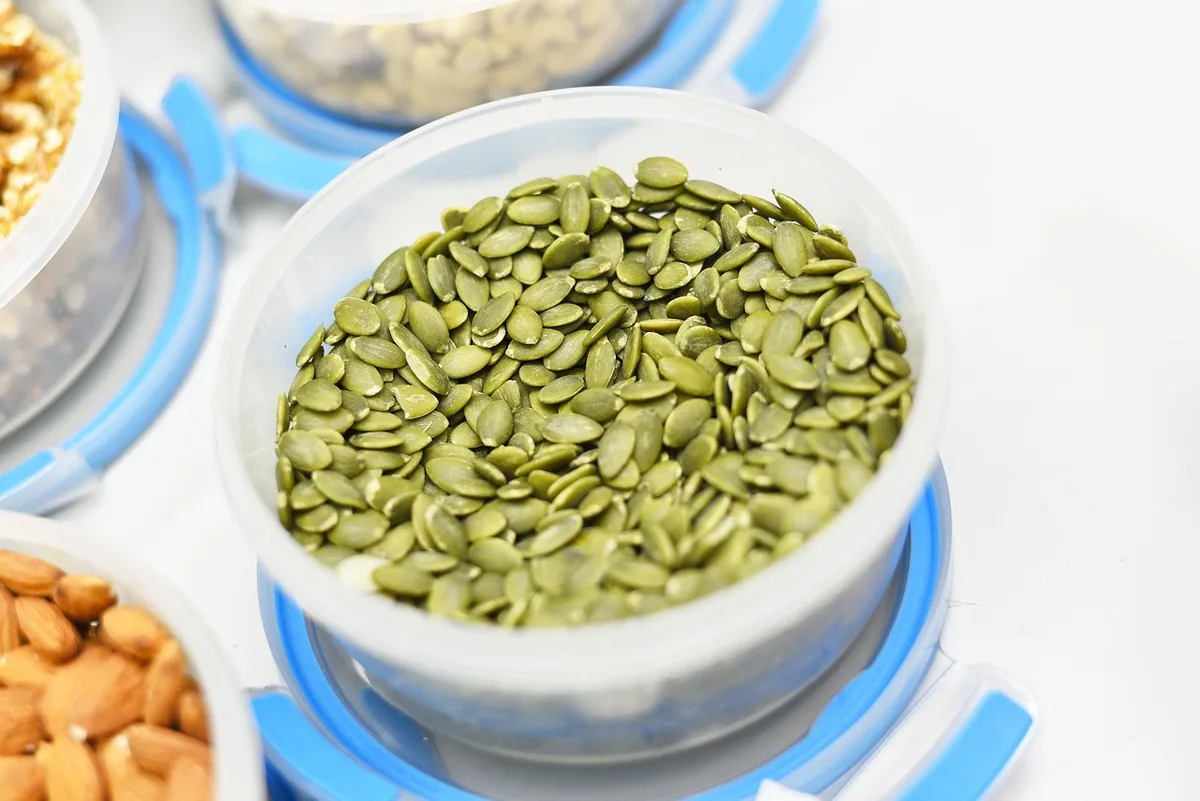 close-up of mixed pumpkin seeds and flax seeds spilling from a small bowl on a wooden table, bright daylight