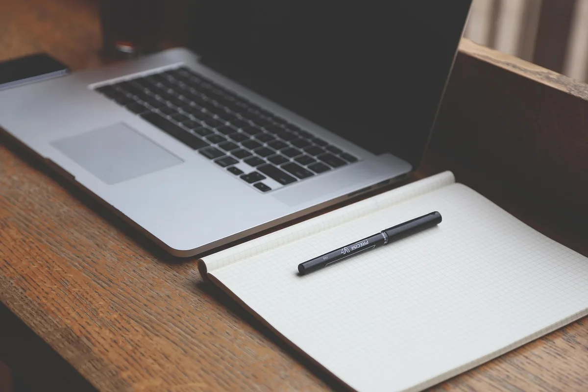 anonymous hands holding a steaming mug beside an open notebook on a bright desk
