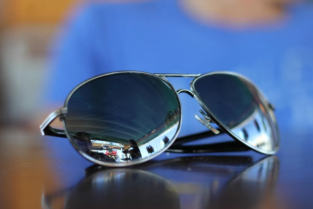 Sunglasses on a café table with a folded soft cloth beside them, bright daylight on the surface, no logos or brands