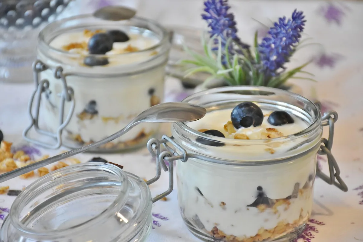 hands stirring a jar of thick unbranded creamy skyr with berries and oats in background, natural daylight kitchen table