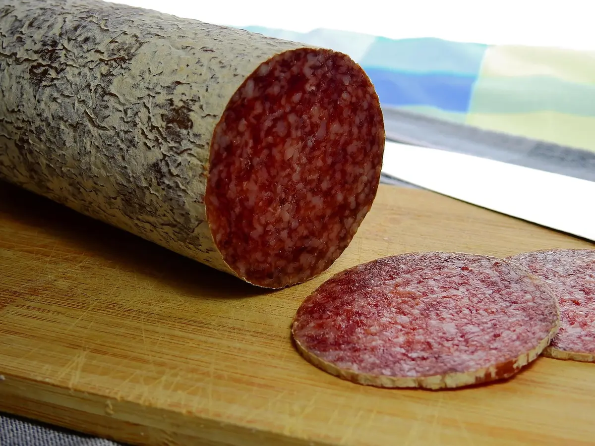Bright kitchen counter with a variety of unbranded cold cuts and a bowl of salad, hands reaching for a fork